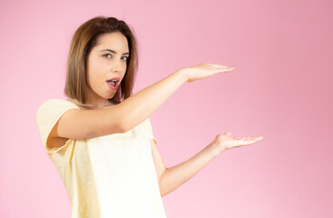 Young woman over isolated pink background holding something with both hands, product presentation.