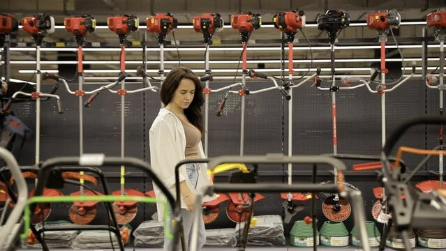 A young woman examines lawn mowers for her garden. Shopping for gardening