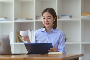 Businesswoman sitting holding a document clipboard while drinking coffee at the table in the office.