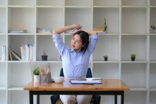 Businesswoman stretching lazy at the desk to relax while working in the office. Feeling stressed and achy from work.