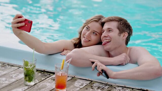 Young lovely couple taking a picture on vacation. Two lovers making selfie together in swimming pool. Boyfriend and girlfriend photographing their honeymoon on resort