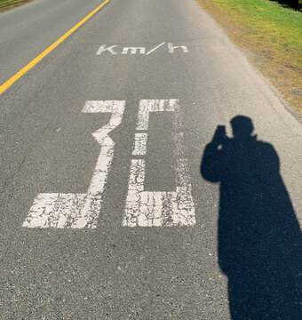 Silhouette of a man standing in a road taking a photo of a 30 km/hr speed limit road marking, British Columbia, Canada