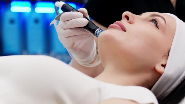 Cosmetology clinic. Professional female cosmetologist doing hydrafacial procedure while being a work. Attractive nice woman lying on the medical bed while having beauty procedures