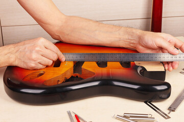 Guitar master measures body of guitar with ruler.