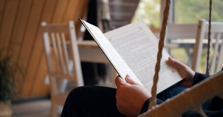 Man reads book, swings on swing in his country house in calm and relaxing atmosphere. quiet reading helps you to be alone with yourself and enjoy silence. cinematic shot man reading book in cozy home