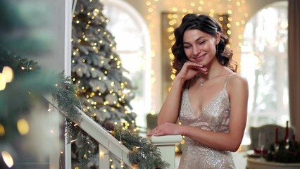 Elegant girl in evening dress smiles and poses for the camera with Christmas lights in the background. Young caucasian woman during New Year's Eve at the party. High quality 4k footage