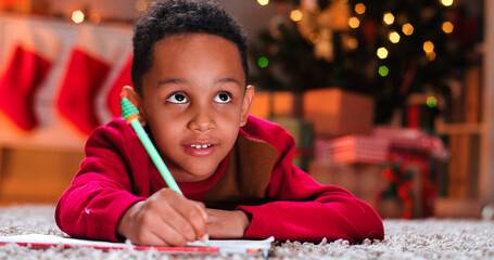 Close up of African American small kid boy on floor drawing and writing on paper in decorated room...