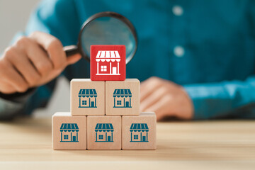 Franchise business concept. businessman holding magnifying glass focus to wooden block with franchise marketing icons.