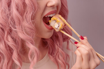 Young woman with red nails and pink hair is eating sushi.