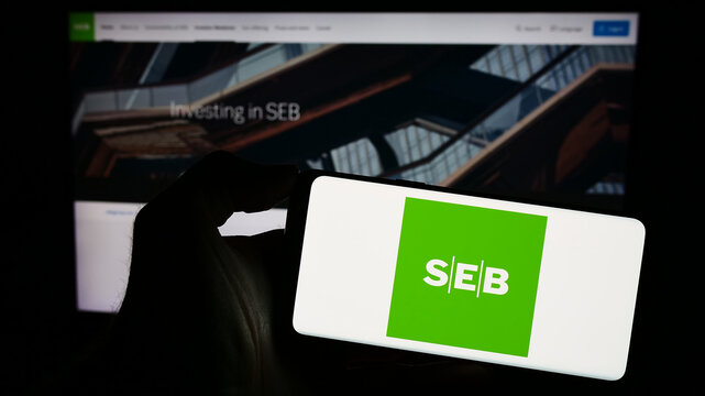 Stuttgart, Germany - 11-17-2023: Person holding smartphone with logo of Swedish company Skandinaviska Enskilda Banken AB (SEB) in front of website. Focus on phone display.