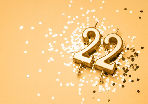 22 years birthday celebration festive background made with golden candle in the form of number Twenty two lying on sparkles. Universal holiday banner with copy space.