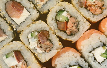 Close-up of a lot of sushi rolls with different fillings lie on a wooden surface. Macro shot of cooked classic Japanese food with a copy space.