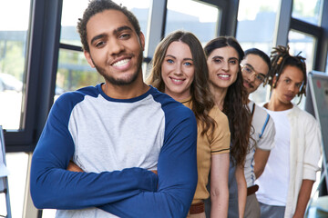 portrait of smiling african american man with folded arms near creative team, confident leadership