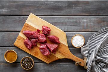 Raw beef meat cutting into pieces on wooden board with spices