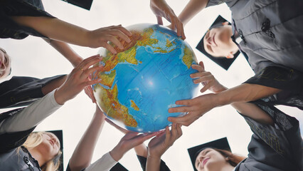 Graduating students twirl a geographic globe of the world in their hands. - obrazy, fototapety, plakaty