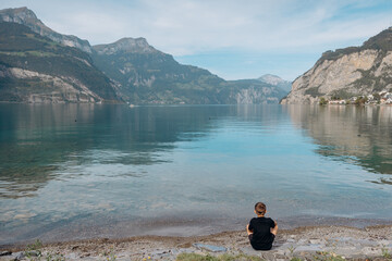 a young man sits on stones on the shore of a lake in Switzerland and looks at the lake