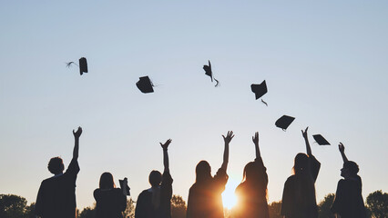 Silhouettes of Happy college graduates tossing their caps up at sunset.