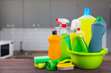 Cleaning products on a wooden table on a blurred kitchen background. Cleaning service concept. Household chemicals.Cleaning and detergents in plastic bottles, sponges and gloves.Mockup. Design. 