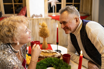 Senior couple sitting at a table by nicely decorated Christmas tree, having fun at Christmas dinner...