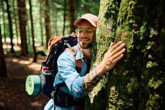 Young backpacker hugging tree while hiking in forest.