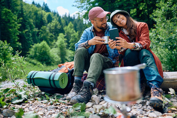 Happy couple using smart phone while camping in nature.