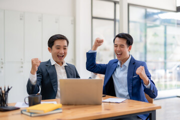 Two asian business man raises her hands up rejoices in increasing profits in business. Asia Businessman is receiving good news online, raising her hands and showing her fists.