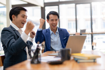 Two asian business man raises her hands up rejoices in increasing profits in business. Asia Businessman is receiving good news online, raising her hands and showing her fists.