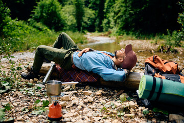 Young backpacker relaxing by mountain creek while hiking in nature.