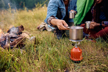 Close up of couple using portable camping stove while relaxing by their tent in nature. © Drazen