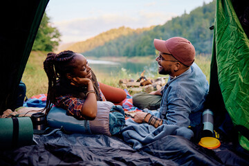 Happy multiracial couple talks while relaxing in tent on camping in nature