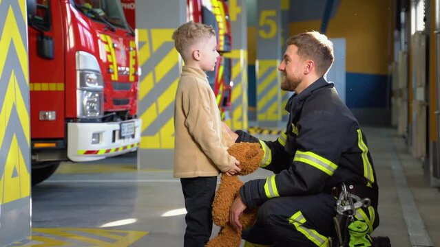 Portrait of rescued little boy with firefighter man standing near fire truck at station