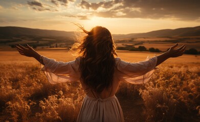 Girl with outstretched arms from the back in a field at sunset