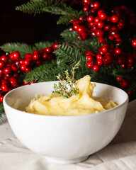 Close-up of white bowl with mashed potatoes, on white tablecloth with Christmas decoration, vertical, with copy space