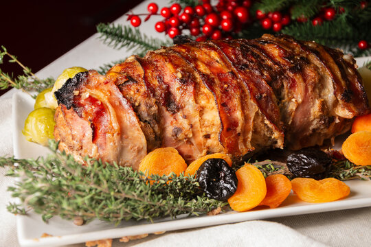 Close-up of turkey stuffed with dried apricots, sauce, potatoes, thyme and pomegranate seeds, with Christmas decoration on white tablecloth, horizontal