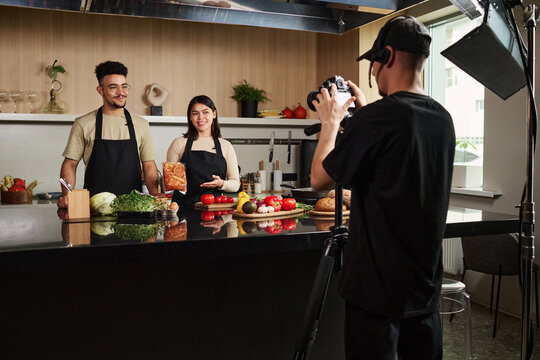 Medium long shot of young middle eastern man and hispanic woman working at studio making culinary show with cameraman filming them