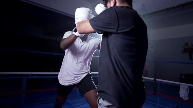 Fighters delivering elbows and legs kicks inside boxing ring. Opponents in heated fight confrontation in training match