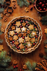 Gingerbread and chocolate tart decorated gingerbread cookies in the star shapes, cranberries and rosemary in a baking dish on a wooden table, top view. Christmas tart. - 685274720