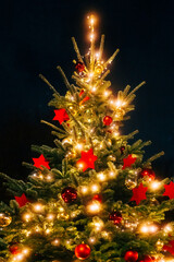 Schön beleuchteter Weihnachtsbaum mit roter und goldener Dekoration mit dunklem Hintergrund bei Nacht und strahlendem Licht