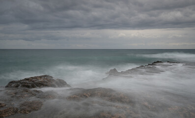 Stormy waves crashing on a rocky shore. Cloudy sky dangerous sea