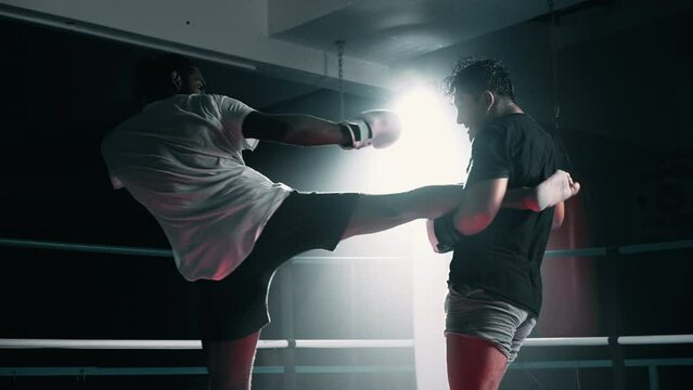 Muay Thai Fighters Exchanging Kicks in Training Match Inside dramatically lit Boxing Ring. Spotlight shining young men fighting