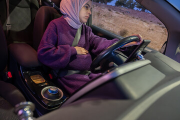 Pregnant arabic muslim woman driving car at night wearing winter clothes ,hijab and seat belt...