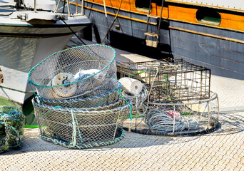 Fishing gear in the form of several baskets and net traps for catching crabs lies on the pier, not far from the boats