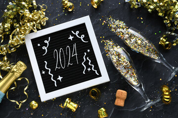 Welcoming 2024 New Year - flat lay champagne glasses bottle gold glitter confetti golden streamers