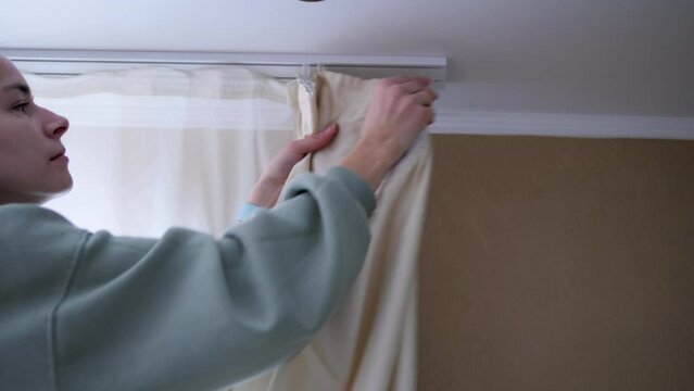 A young girl attentively fixes curtains on special fasteners, adding coziness and style to the room