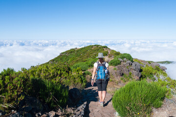 Paisaje de montaña con nubes y niebla al fondo con una senderista recorriendo una levada en Madeira, Portugal.