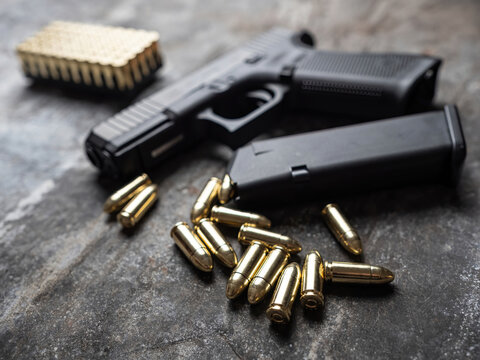 Hand gun with ammunition on dark background. 9 mm pistol military weapon with pile of bullets ammo and cartridge at the metal table.