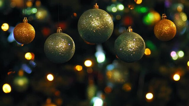 Gold and silver Christmas balls rotate against the backdrop of glowing Christmas garlands on the Christmas tree in blur. Medium plan