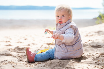 An adorable little toddler is walking along an empty cold beach with a duck toy, a beautiful landscape and a cute childhood concept
