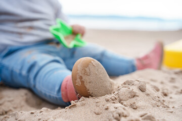 A little toddler is playing with sand and a shovel outside - obrazy, fototapety, plakaty