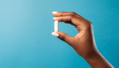 female hand holding white capsule on blue background close copy space pharmacology concept - obrazy, fototapety, plakaty
